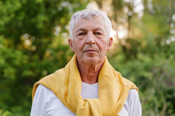 Senior man with grey hair and a yellow sweater draped over his shoulders, looking directly at the...