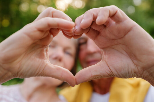 A blurred senior couple is in the background while their hands form a heart shape in sharp focus in the foreground, symbolizing love and connection.