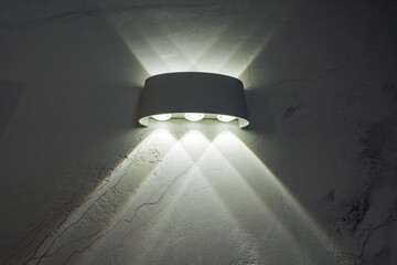 A bright white wall light is illuminating a dark wall, creating a striking contrast that enhances...