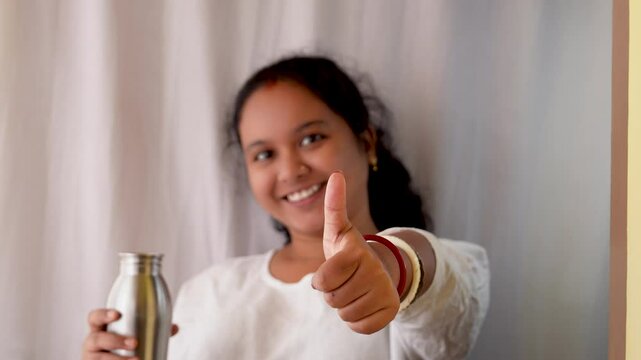 A young Indian woman pointing towards a stainless steel bottle in hand on white background.