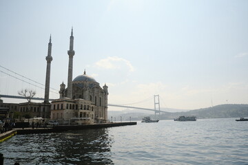 Naklejka premium Historic mosque overlooks the Bosphorus with a bridge in the background on a sunny day in Istanbul
