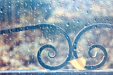 raindrops on glass blurred autumn background trees in the park, seasonal backdrop rainy weather