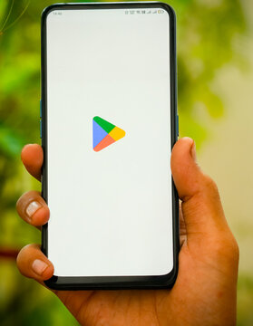 INDIA, DELHI - MAY 16, 2025:Google Play Store launch screen on mobile phone held vertically by hand with lush green outdoor background, showcasing Android digital store app.