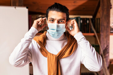 Quarantine. Indian Teacher Man Wearing Protective Face Mask Standing Near Blackboard With English...