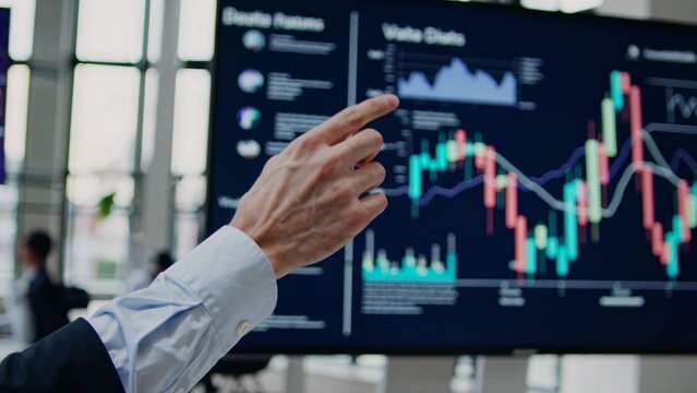 Business coach pointing at interactive screen showing candlestick chart, explaining company revenue and profit growth, financial analysis and investment strategy