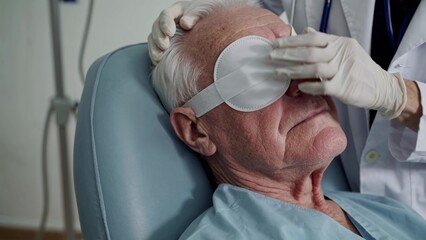 Doctor carefully placing eye patch on senior male patient after ophthalmology surgery, ensuring comfort and promoting healing in hospital setting