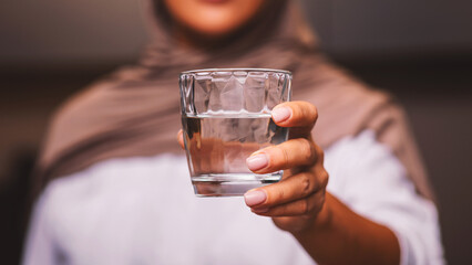 Unrecognizable Muslim Woman Offering Glass Of Water To Camera Standing In Modern Kitchen At Home, Wearing Hijab. Healthy Hydration, Drink More Water And Stay Hydrated. Selective Focus, Cropped
