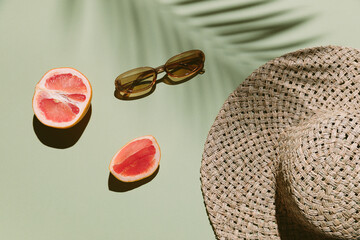 Summer flat lay with straw hat, sunglasses and grapefruit on green background with palm leaf...