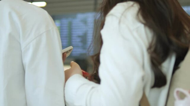 Man and a woman are looking at a screen with a phone in the man's hand. The man is wearing a white shirt and the woman is wearing a white shirt and a backpack