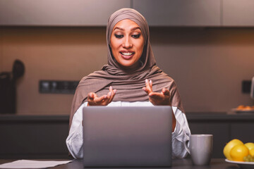 E-Teaching. Arab Lady Making Video Call On Laptop Talking Teaching Online Sitting In Modern Kitchen...