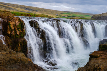 Kolugljufur Canyon showcases stunning waterfalls cascading over rugged cliffs. Lush greenery thrives along the banks, creating a peaceful atmosphere. Ideal for nature enthusiasts and photographers.