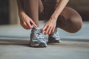 Close-up of female runner tying shoelaces on running sneakers before summer workout in the city –...