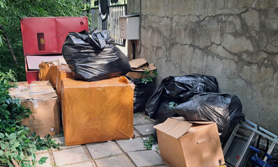 Discarded cardboard boxes and garbage bags piled near a wall in an urban backyard