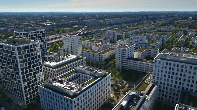 Aerial view of modern buildings near Hirschgarten in Munich, Germany, featuring green rooftops, residential towers, and office blocks surrounded by trees and urban infrastructure. 30 September 2024.