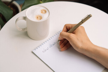 Handwriting slow down in notebook next to a mug of cappuccino on a round table. High quality photo