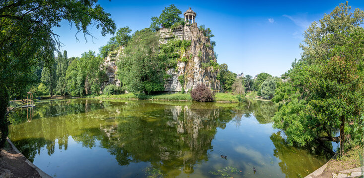 Paris, France - 06 14 2025: Buttes-Chaumont Park. View the central part of the park with belvedere island, Temple of the Sibyl, the lake, remarkable trees and vegetation