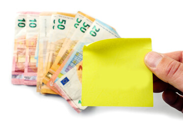 European banknotes on a white surface and hand holding yellow paper note on top. Monthly bill payments reminder for house rent, electricity, water and phone. Rising cost of living in Euro Union.