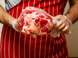 Fresh juicy leg of lamb with bone in a butcher hands. Red and white stripe apron background. Selective focus. High quality and price meat product. Agriculture and food industry.
