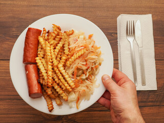 A plate of food with a hot dog and French fries on it and sauerkraut salad is placed on the wooden...