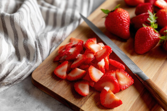 Sliced strawberries arranged on a wooden cutting board beside an old knife for culinary preparation