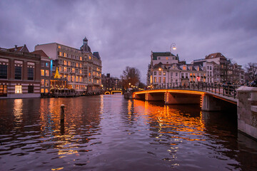 Obraz premium A picturesque canal scene in a city Amsterdam, showcasing a row of tall, narrow buildings with traditional European facades. Several houseboats are moored along the water.