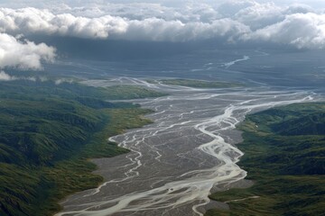 Aerial view of a braided river system carving through a green landscape under a cloudy sky