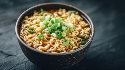 A rustic bowl holds steaming noodles in a flavorful broth, garnished with vibrant green onions. The warm dish is presented on a dark textured surface, creating a cozy atmosphere