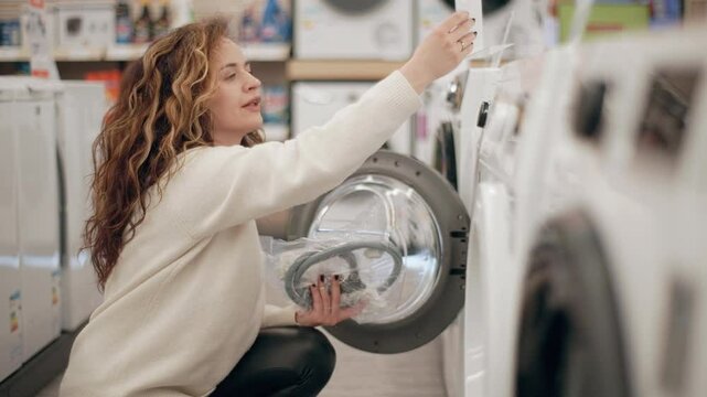 Customer carefully examining washing machines in electronics store, comparing features and specifications while browsing product display in slow motion, exploring potential home appliance purchase