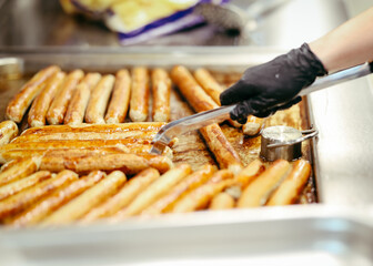 Traditional German sausages being grilled on a large tray in a professional kitchen, flipped by a...