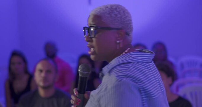 Close up of African American woman preaching into microphone during evangelical service, speaking passionately to Hispanic and Latin audience in church setting