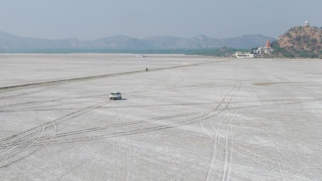 Aerial drone shot of a vehicle moving through the flat, horizon-stretching landscape of the Rann of Kutch.