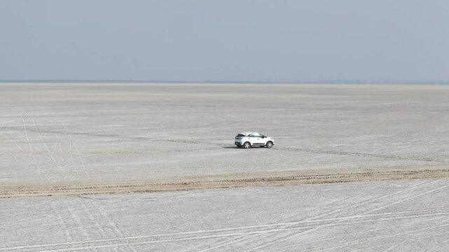 Aerial drone shot showing a white car driving under the vast sky over the Rann of Kutch salt desert.