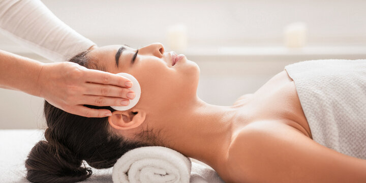 Professional Cosmetologist Cleansing Skin Of Young Asian Woman During Facial Beauty Treatments In Spa, Relaxed Korean Lady Enjoying Wellness Day At Beauty Parlor, Lying In Massage Table, Side View