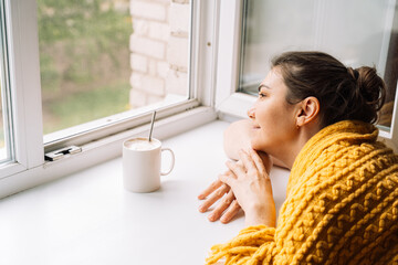 Woman relaxing with a cup of coffee near the window, wrapped in a yellow sweater. High quality photo