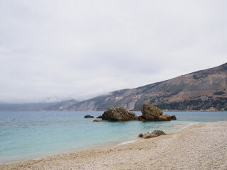 Stormy beach image from Kefalonia with large rock in sea and overcast sky, ideal for seasonal...