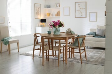 Dining table with beautiful flowers and dishware in room. Interior design