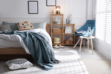 Cozy bed with soft linens, furniture and decor in stylish room. Home textile
