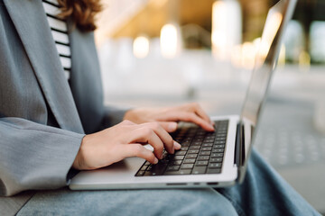 Close-up of businesswoman's hands typing on laptop against outdoor background. Woman working on...