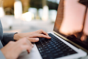 Close-up of businesswoman's hands typing on laptop against outdoor background. Woman working on...