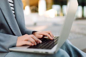 Close-up of businesswoman's hands typing on laptop against outdoor background. Woman working on...