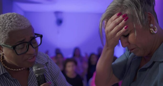 Emotional moment in evangelical church as woman prays in tears, receives support through hand holding, and shares heartfelt embrace during spiritual breakthrough