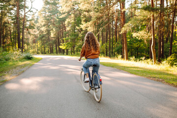 Happy woman riding a bicycle along a path in the forest in the rays of the sun. Beautiful woman...