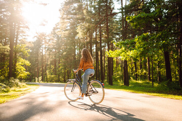 Happy woman riding a bicycle along a path in the forest in the rays of the sun. Beautiful woman...