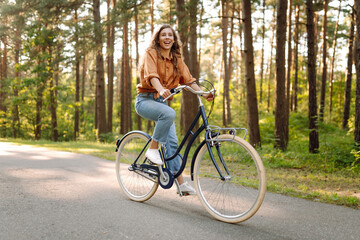 Happy woman riding a bicycle along a path in the forest in the rays of the sun. Beautiful woman...