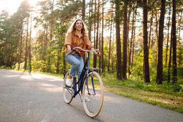Happy woman riding a bicycle along a path in the forest in the rays of the sun. Beautiful woman...