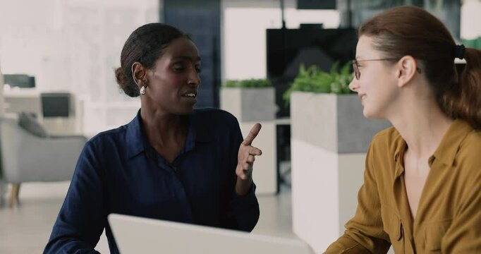 Positive confident African American business professional advisor woman talking to colleague, employee, intern at workplace, pointing at laptop, giving consultation about online project, task
