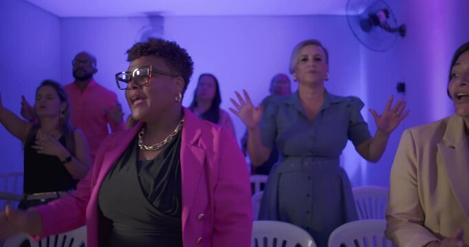 Congregation singing and clapping during evangelical church service in small indoor room with joyful expressions and devotional energy among diverse group of worshippers