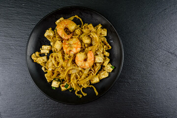 Black plate with pad thai on a slate board. Top view