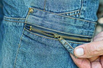 hand unzip iron with slider zipper on pocket of fashionable stylish blue worn men's striped and buttoned denim summer elegance shorts