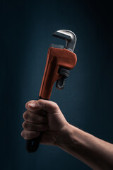 Adjustable pipe wrench in male hand on dark blue background.
